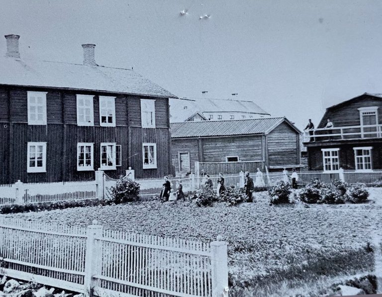 Historiskt fotografi av trähus och människor i en trädgård i Luleå, en av släktens platser